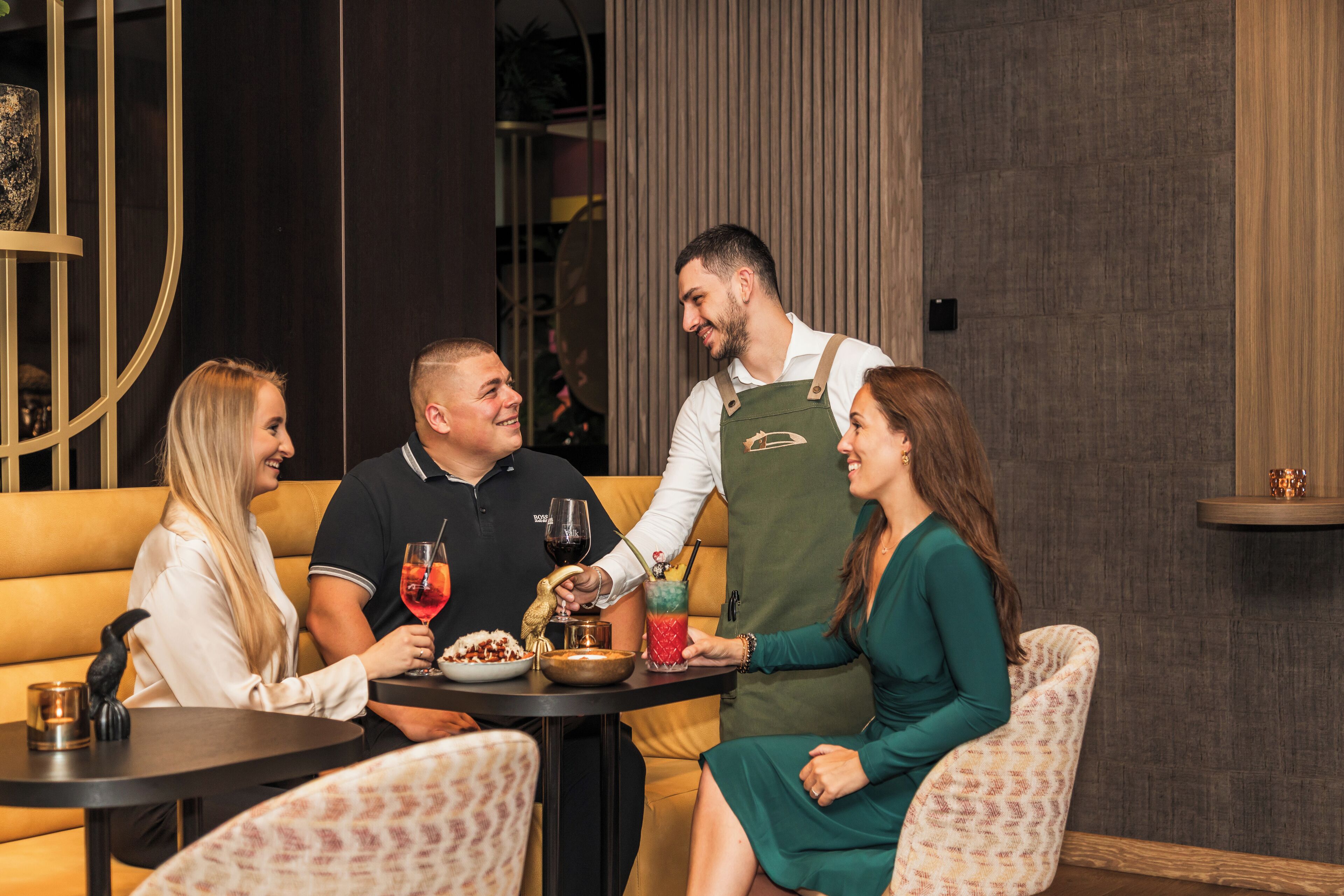 A group of people seated at a table in a restaurant with a modern interior, including a sofa and a wooden accent wall.