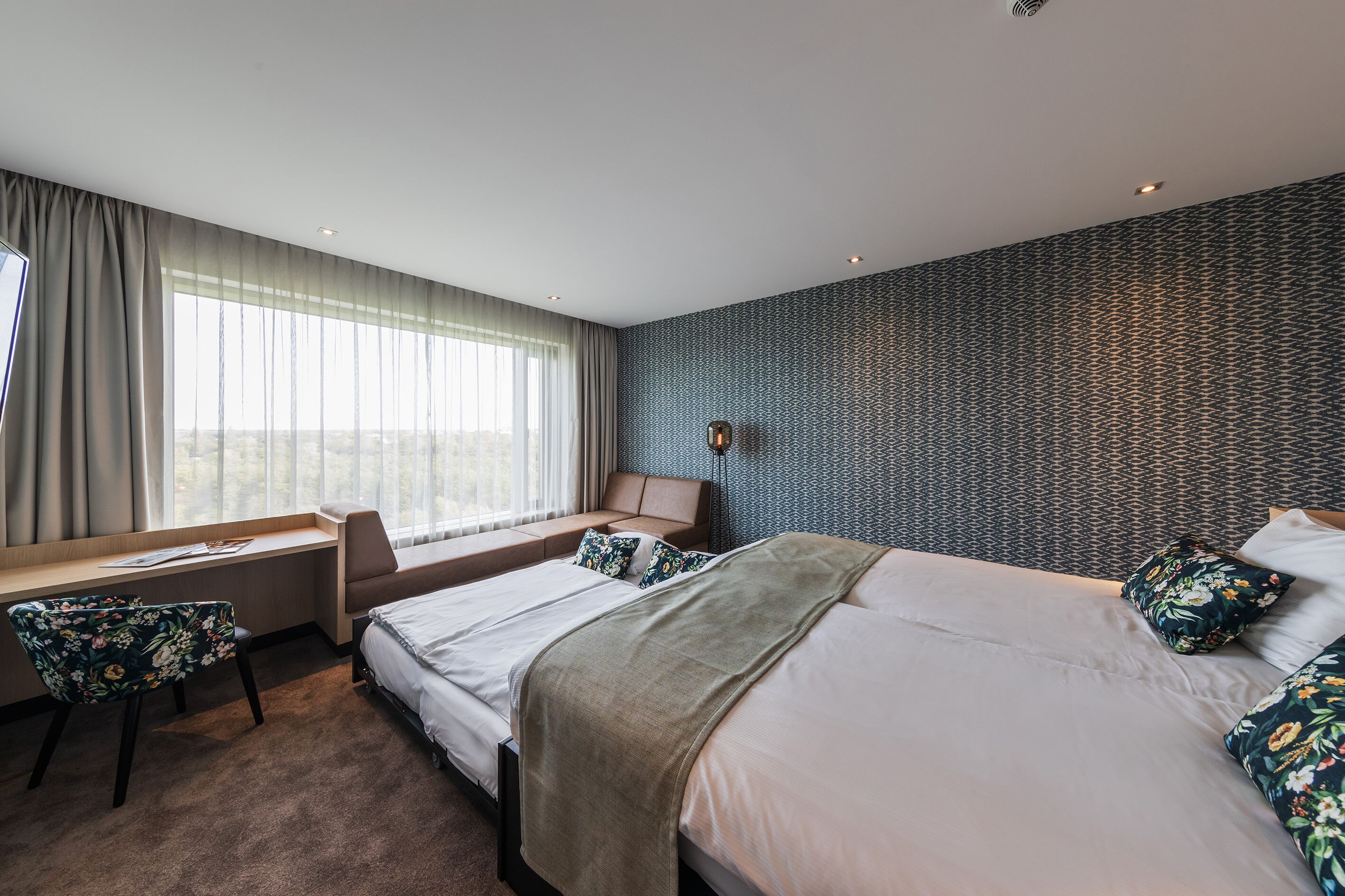 A hotel room with a large bed, a desk with a chair, and a view of the outdoors through the window.