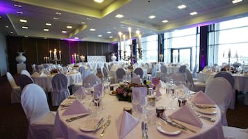 A banquet hall with round tables set for a formal event, featuring white tablecloths, silverware, and candle centerpieces.