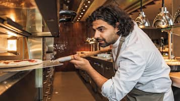 Une cuisine équipée d’appareils électroménagers en acier inoxydable, une personne utilisant une pelle à pizza et un éclairage au plafond.