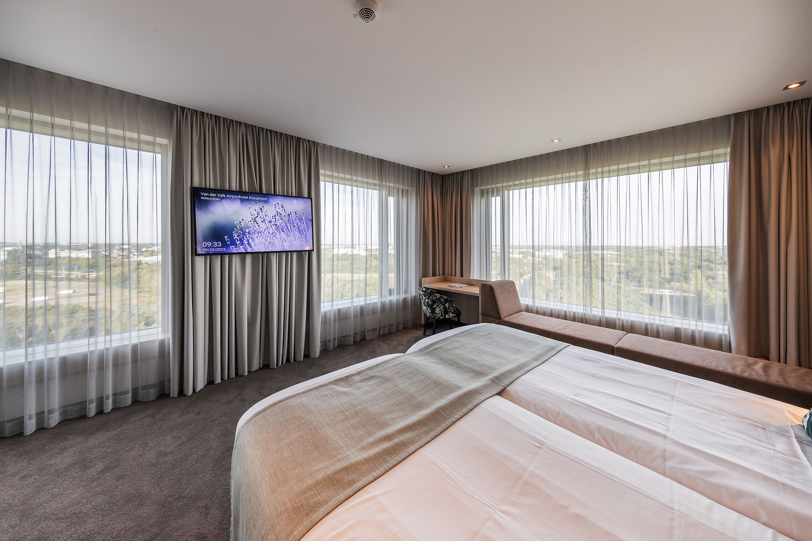 Ein Hotelzimmer mit einem großen Bett, einem Schreibtisch und einem an der Wand befestigten Fernseher.