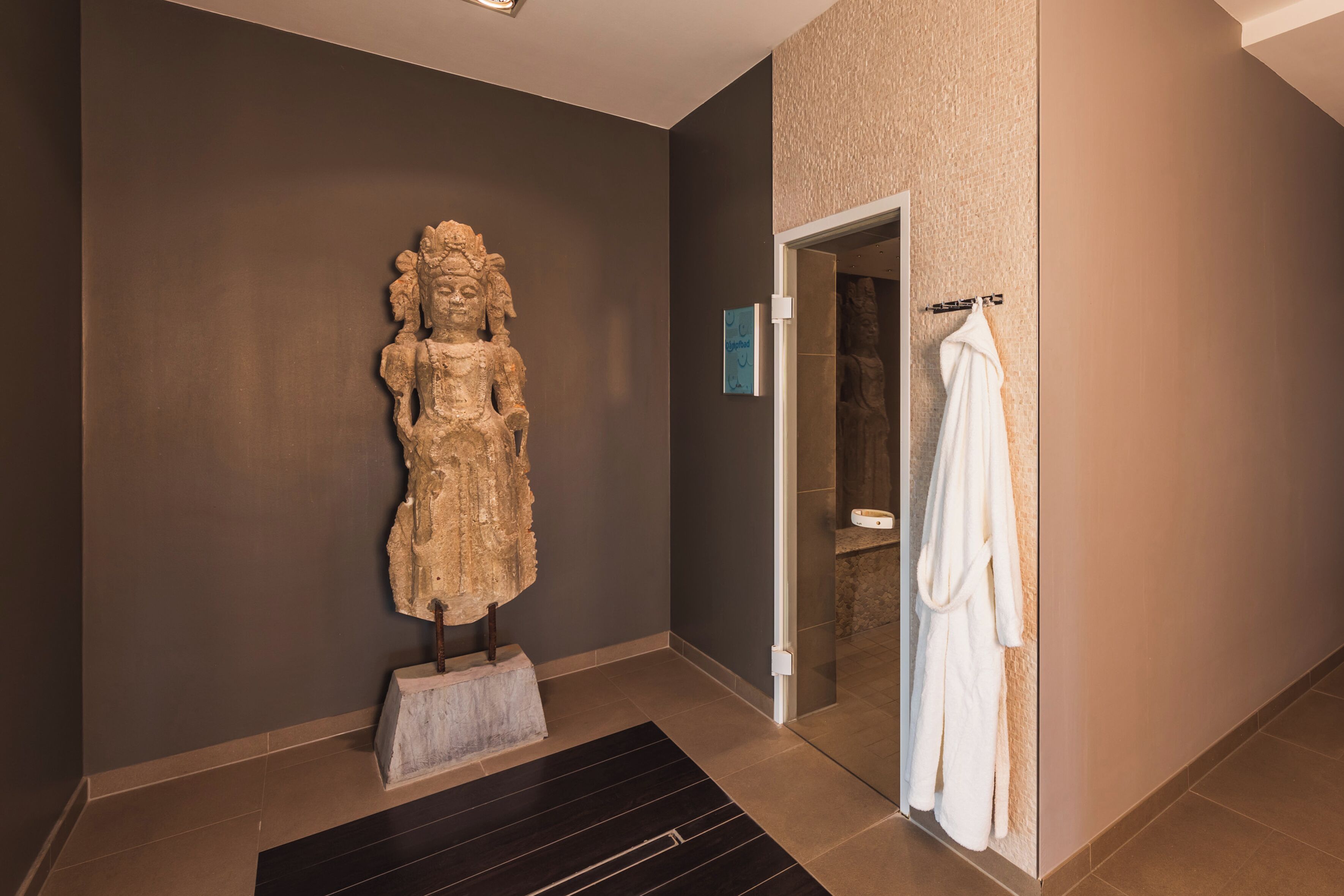 Une statue dans un couloir, une robe suspendue à un portant et une porte donnant sur une salle de bain.