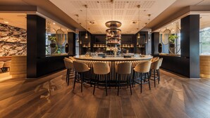 Zona de bar moderna con barra central, diversas opciones de asientos y techo decorativo.