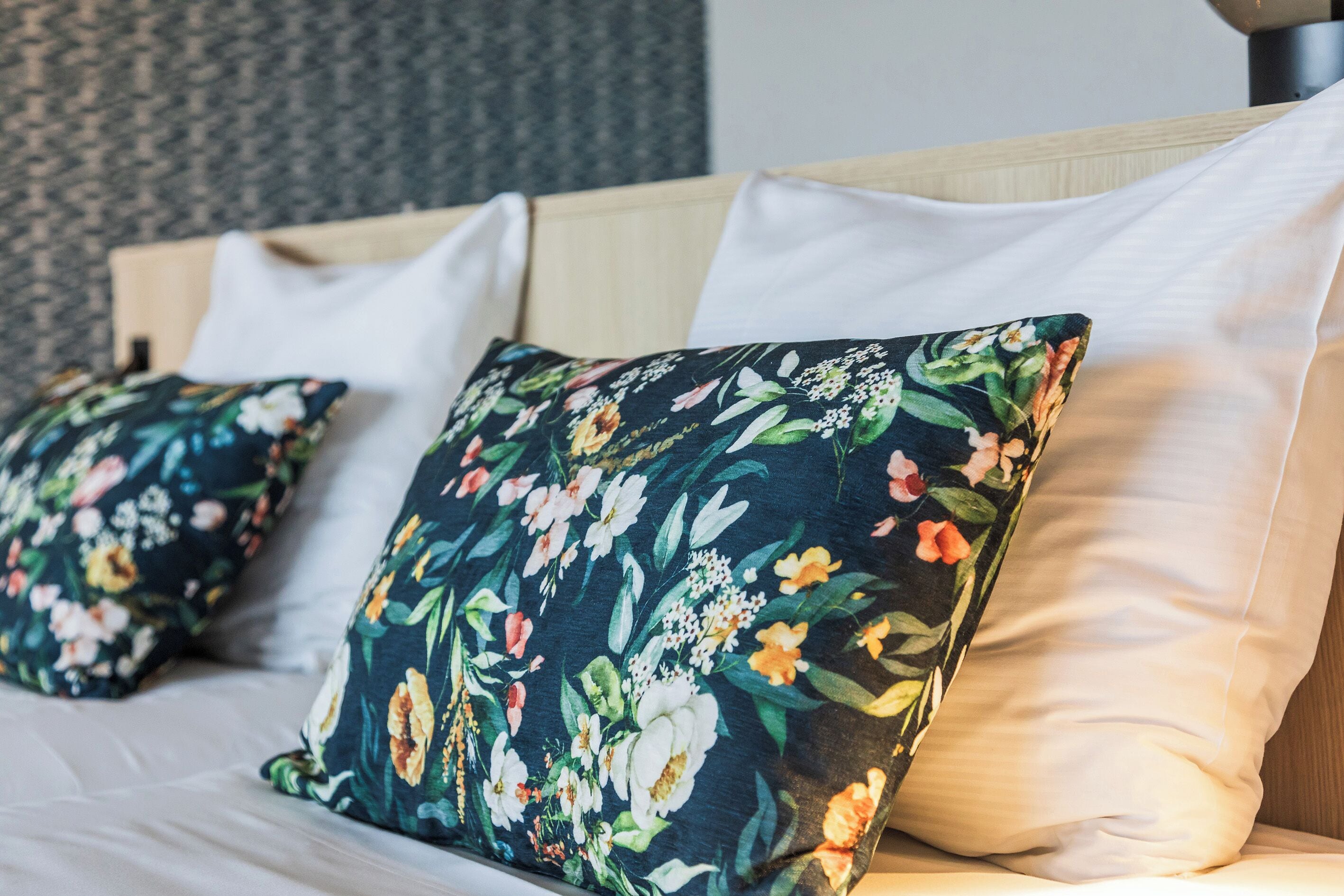 A bed with white linens and floral-patterned pillows.
