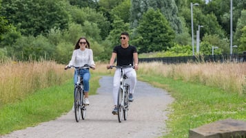 Two people riding bicycles on a paved path surrounded by greenery.
