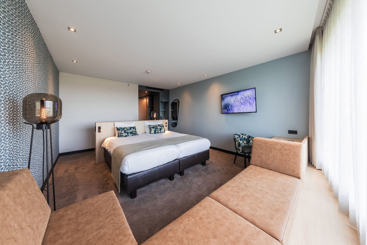 Une chambre d’hôtel moderne avec un grand lit, un coin salon et un téléviseur fixé au mur.