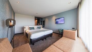 A modern hotel room with a large bed, a seating area, and a television on the wall.