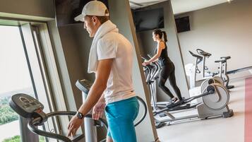 Una palestra con tapis roulant e attrezzature per esercizi, ampie finestre con vista sul verde e un design moderno.