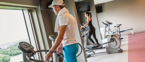 Una palestra con tapis roulant e attrezzature per esercizi, ampie finestre con vista sul verde e un design moderno.