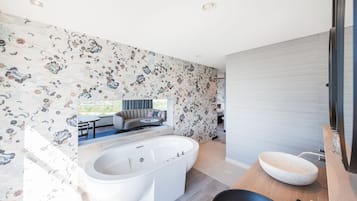 Um banheiro moderno com uma banheira de pedestal, uma pia grande e vista para uma sala de estar com sofá e mesa de jantar.