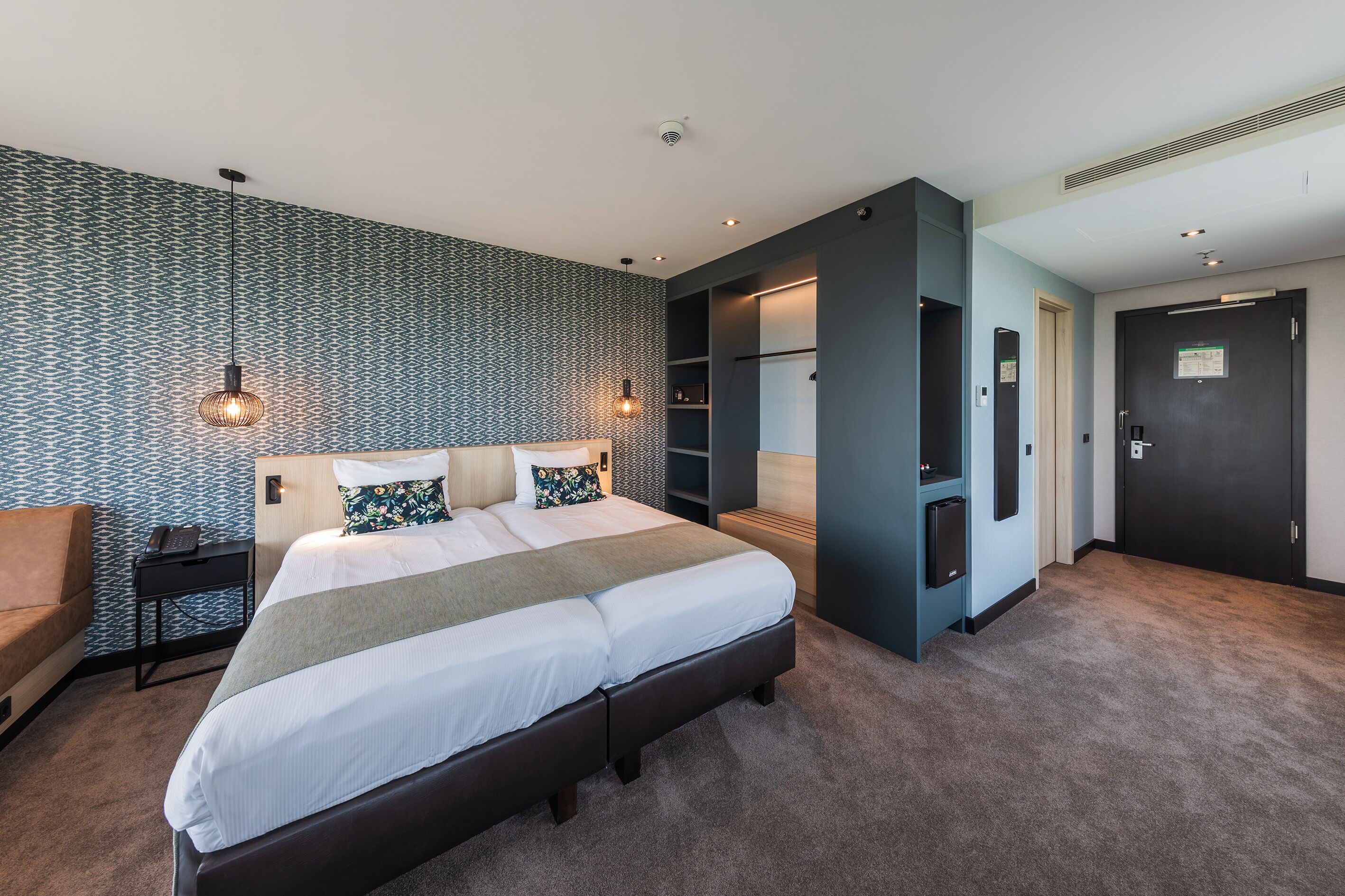 A modern hotel room with a large bed, built-in shelving, a desk, and a wardrobe.