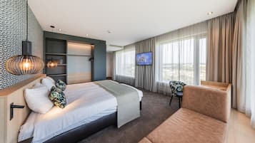A modern hotel room with a bed, a sofa, a TV, and a city view.