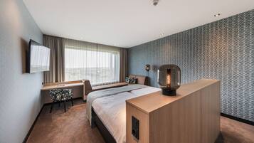 Ein modernes Hotelzimmer mit Bett, Schreibtisch, Stuhl und einem großen Fenster.
