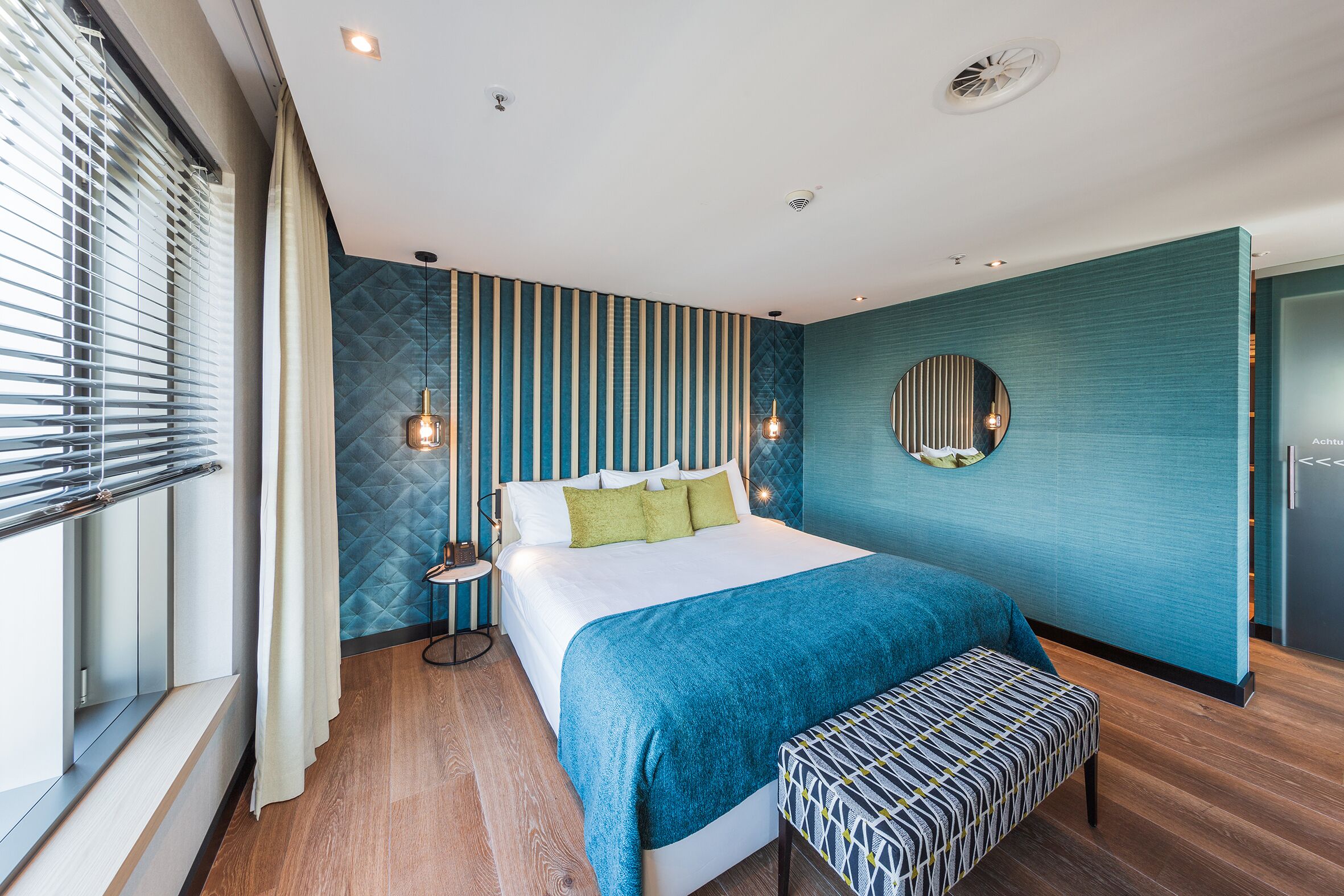 A modern bedroom with a large bed, a bench, and a circular mirror on the wall.