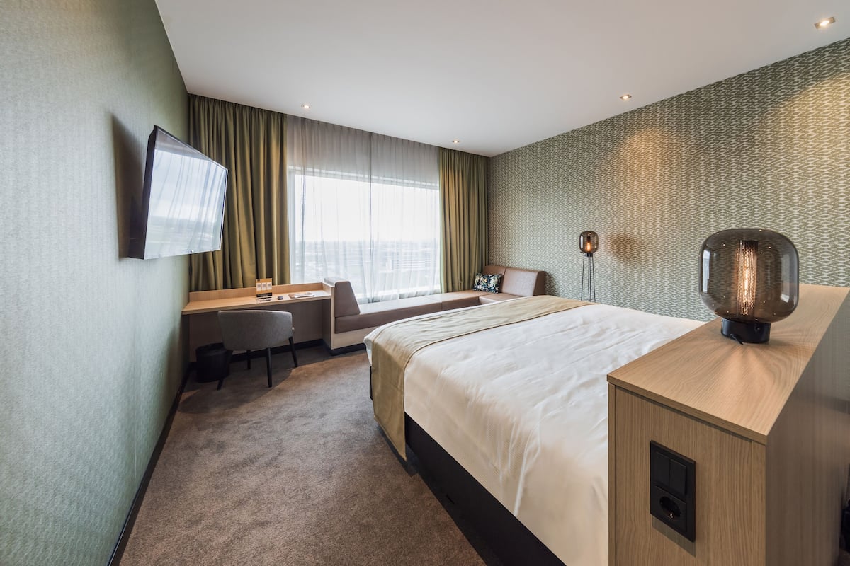 A hotel room with a bed, a desk, a chair, a television, and a decorative lamp.
