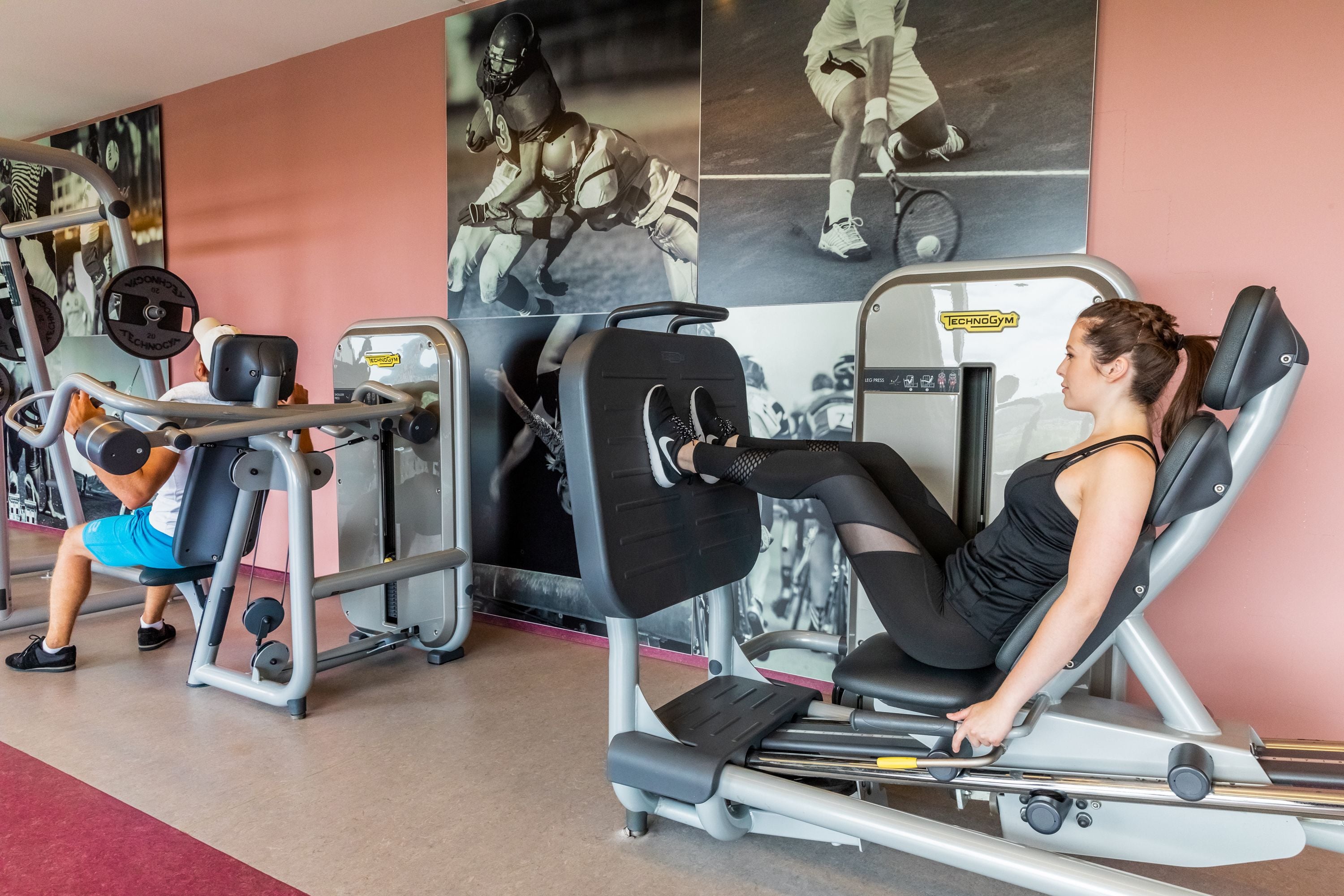 Uma academia com equipamentos de ginástica, incluindo uma máquina de leg press e uma máquina de leg press sentada.