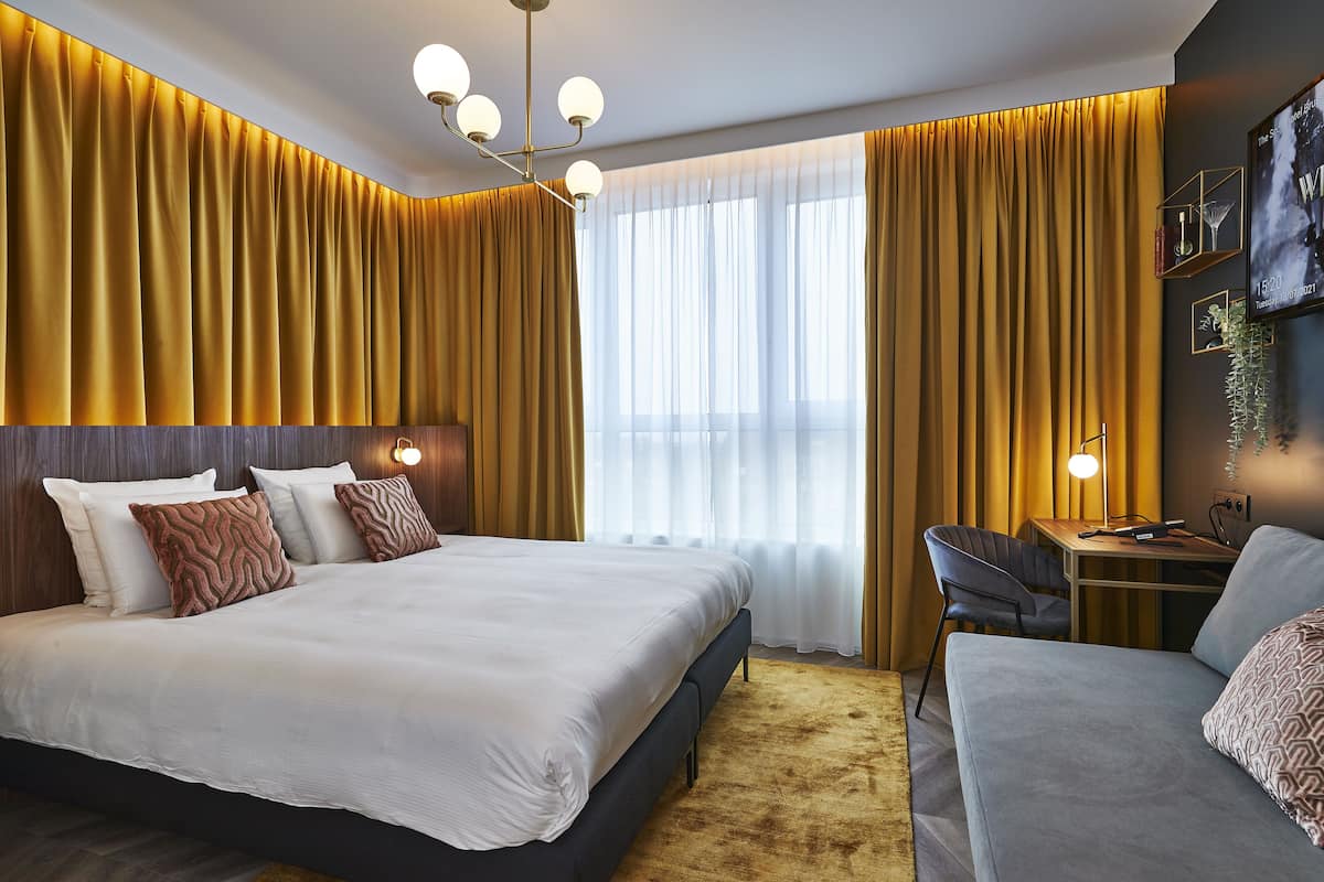 A modern hotel room with a large bed, a desk, and a sofa.