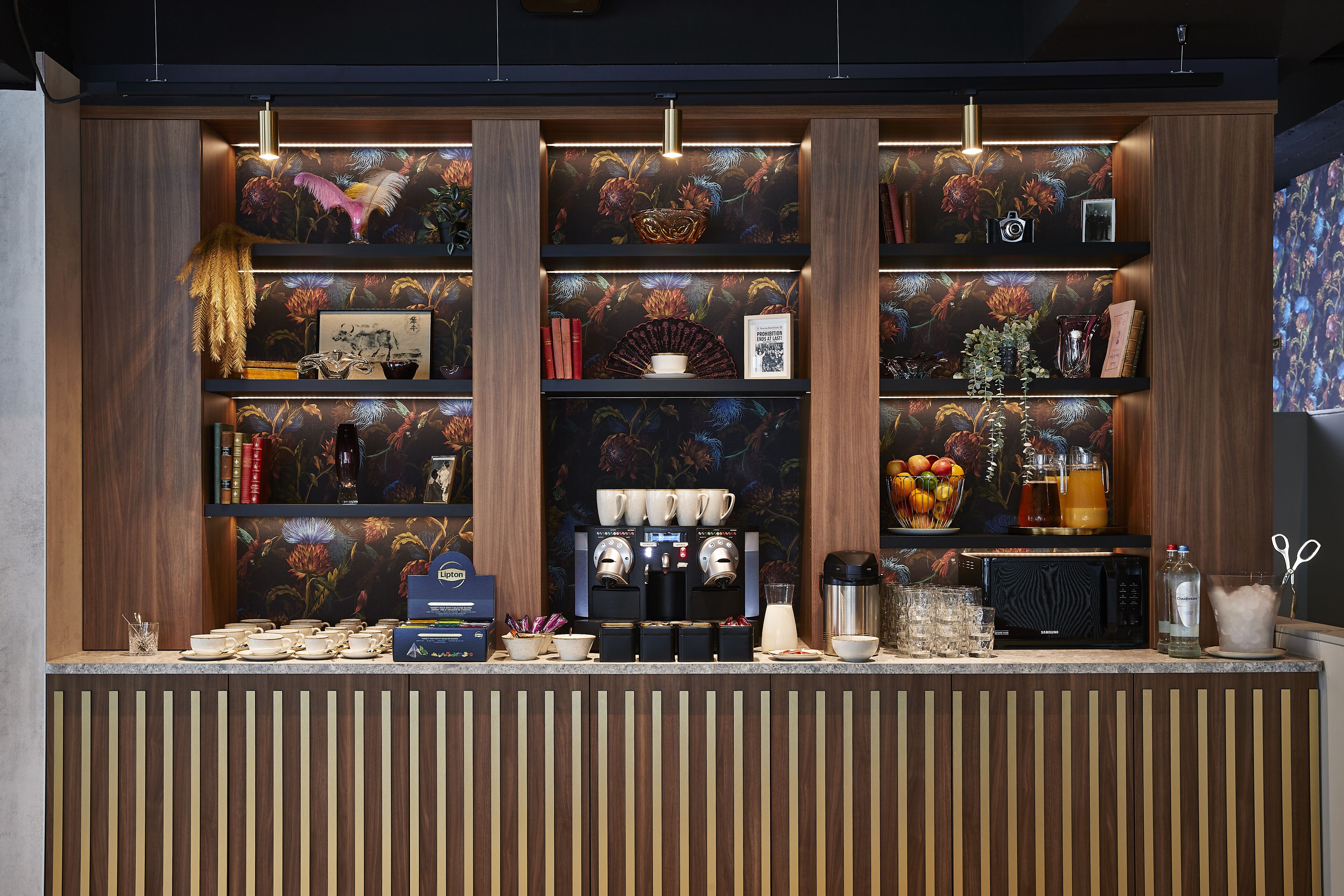 A coffee station with multiple coffee makers, cups, and a fruit bowl.