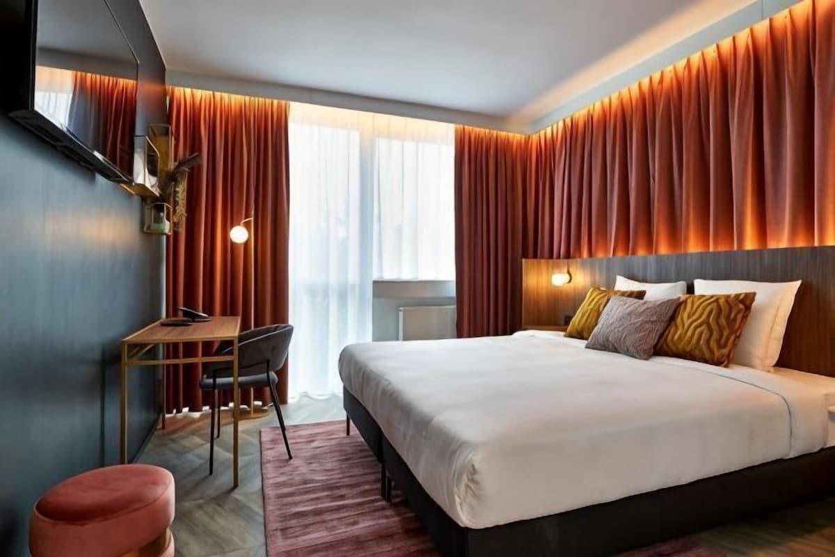 A modern hotel room with a large bed, a desk, and a chair.