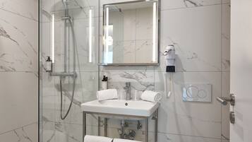 Ein modernes Badezimmer mit einer gläsernen Duschkabine, einer marmorierten Wand, einem weißen Waschbecken und einer Toilette.