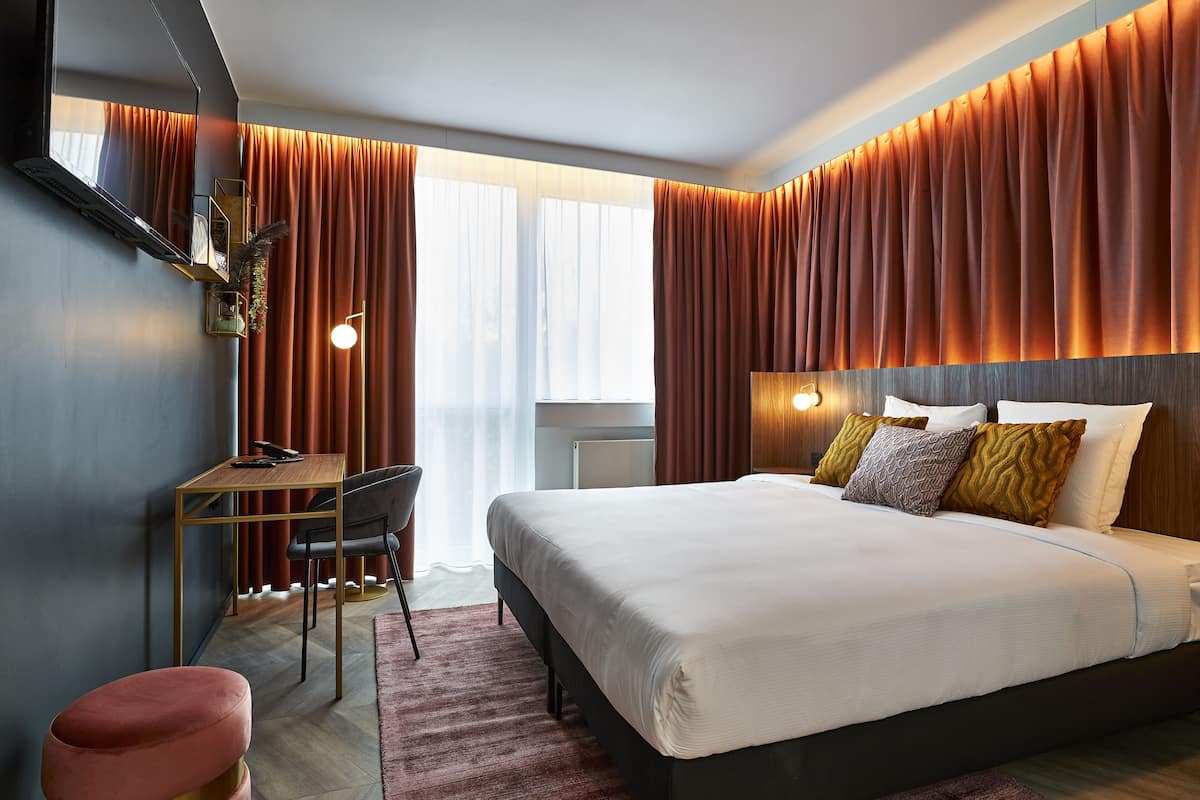 A modern hotel room with a large bed, a desk, and a chair.