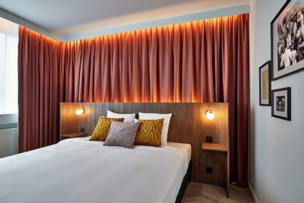 A hotel room with a large bed, two bedside tables, and a headboard with integrated lighting.