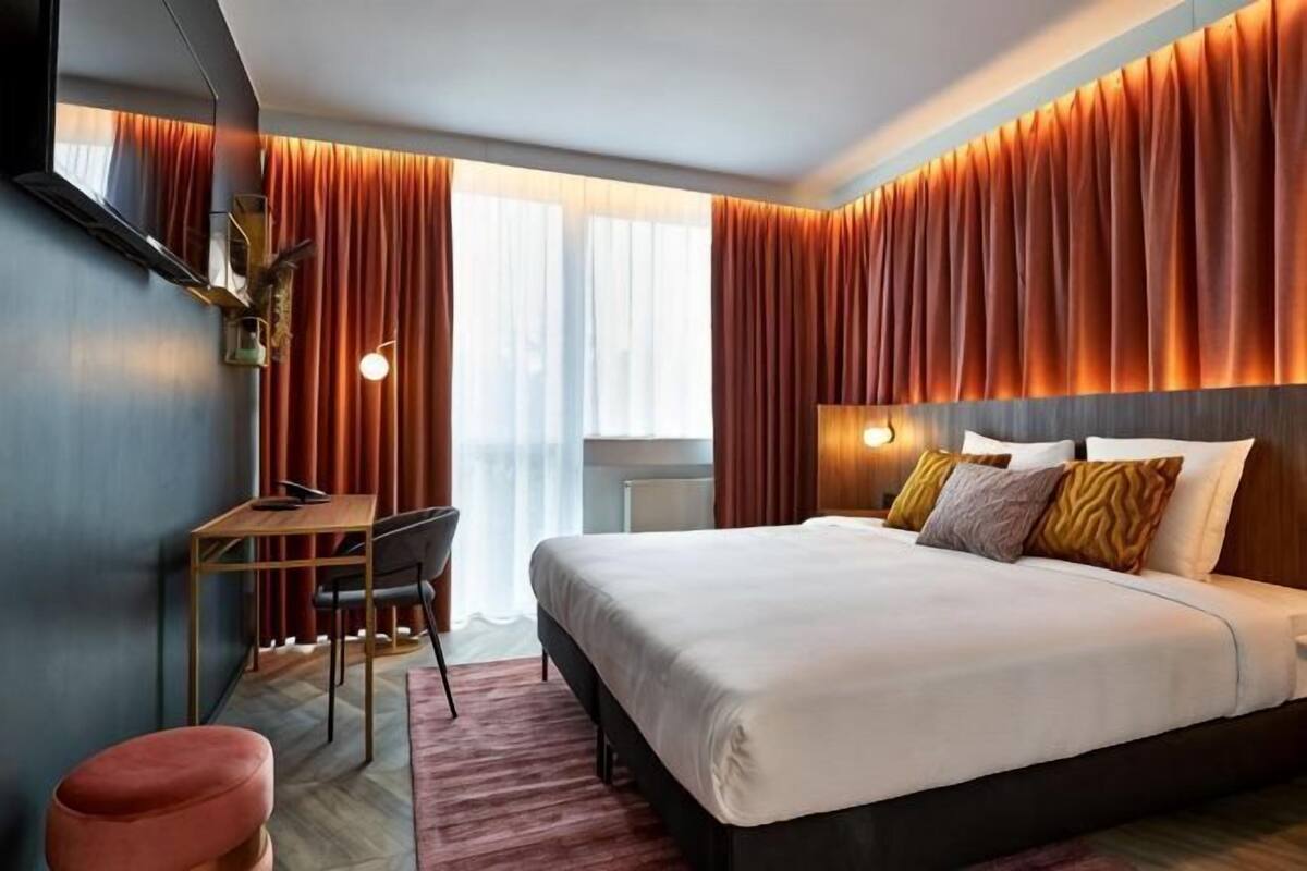 A modern hotel room with a large bed, a desk, and a chair.