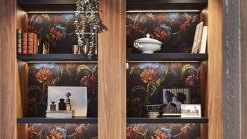 Un interior de madera con estanterías mostrando libros, adornos y un diseño de papel tapiz floral.