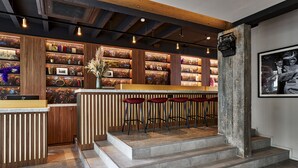 A modern bar area with wooden shelves, red bar stools, and a concrete staircase.
