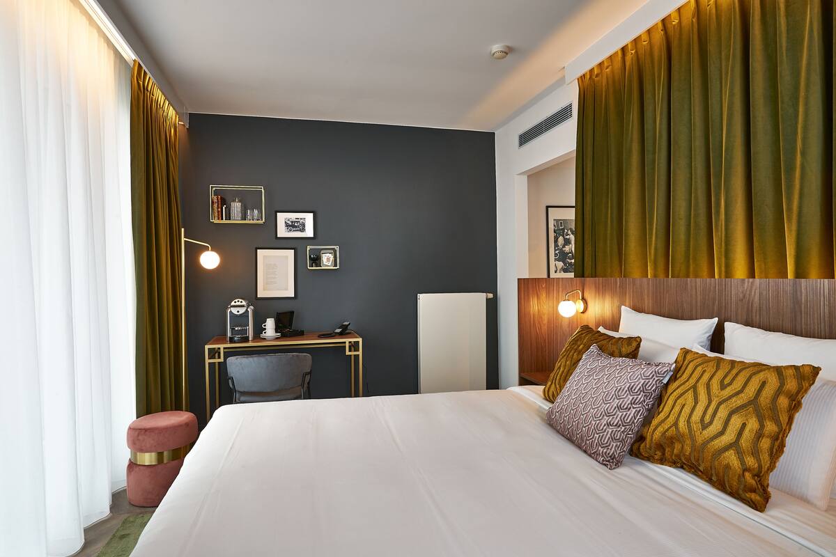 A hotel room with a bed, desk, chair, and a wall with framed pictures.