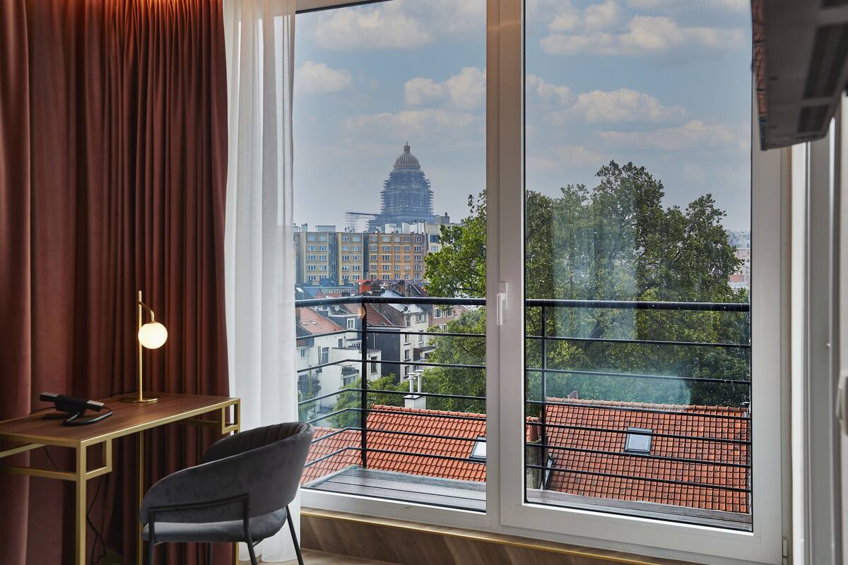 A room with a large window, a desk with a lamp, and a chair.