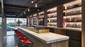 A modern bar area with a long counter, multiple stools, and a wooden panel wall with illuminated shelves.