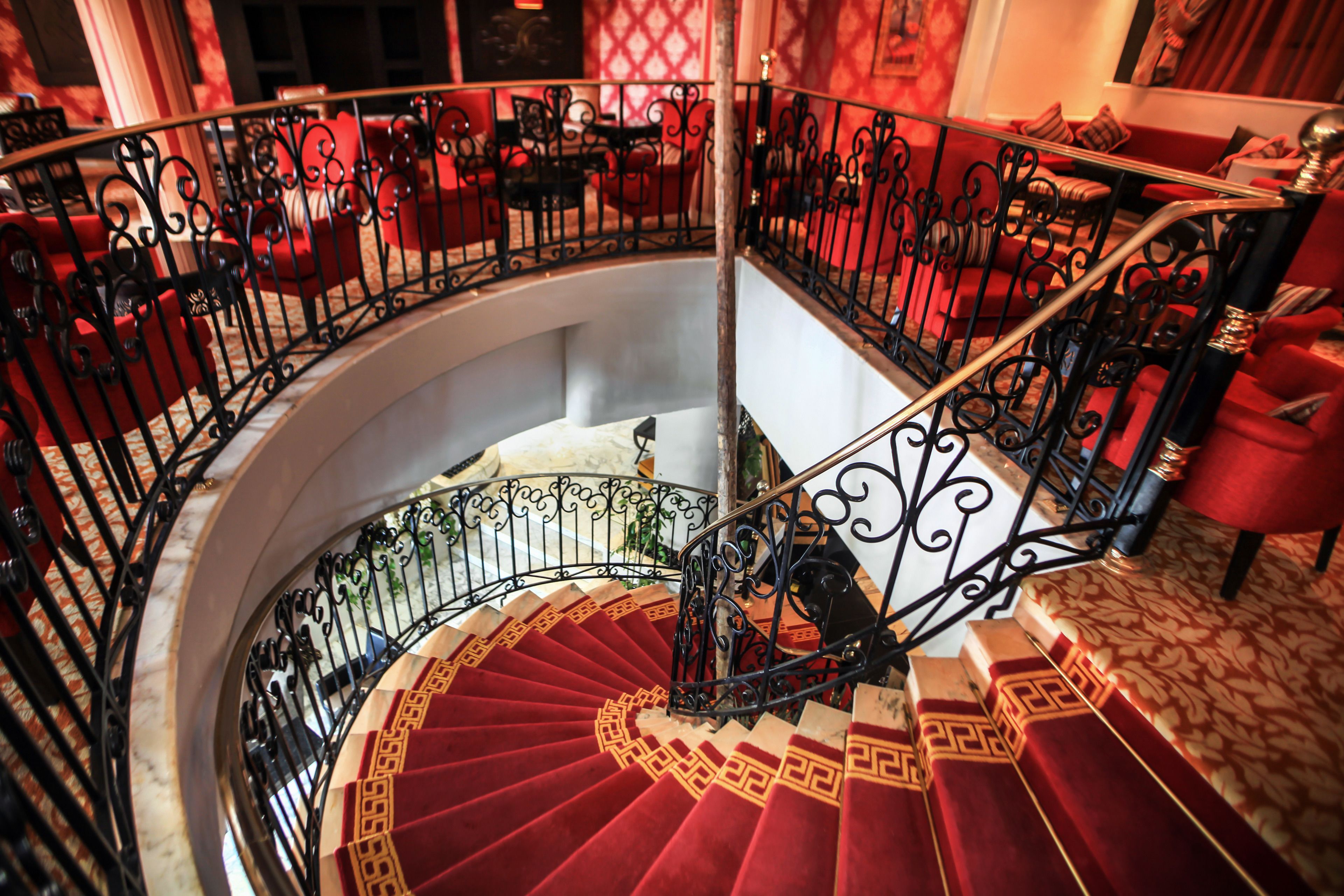 Una gran escalera en espiral con barandillas negras ornamentadas y peldaños alfombrados en rojo.