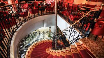 Una gran escalera en espiral con barandillas negras ornamentadas y peldaños alfombrados en rojo.