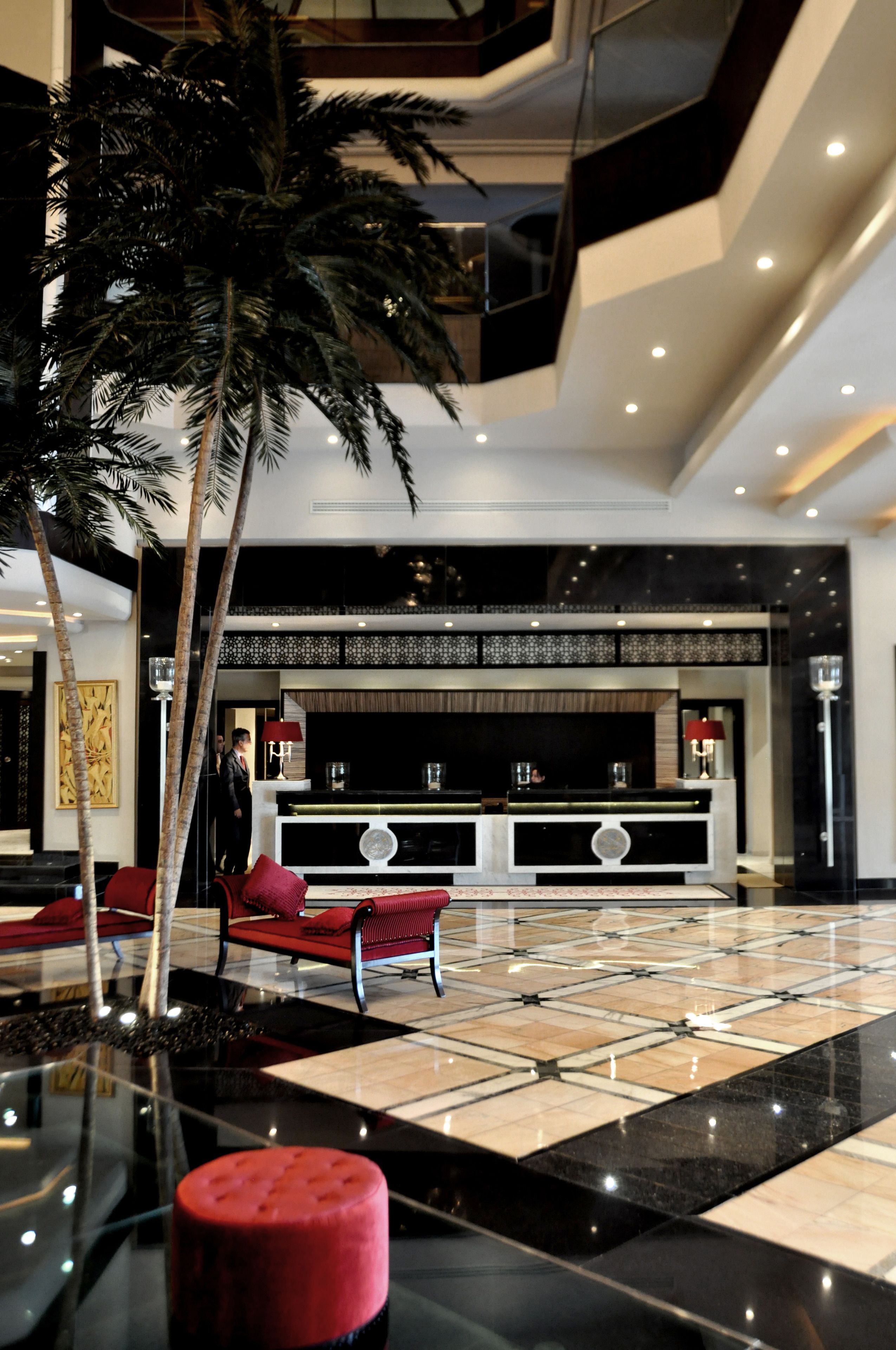 Un vestíbulo con palmera, asientos rojos, mostrador de recepción y diseño moderno.