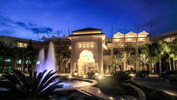 A hotel with a central fountain, palm trees, and a well-lit entrance.
