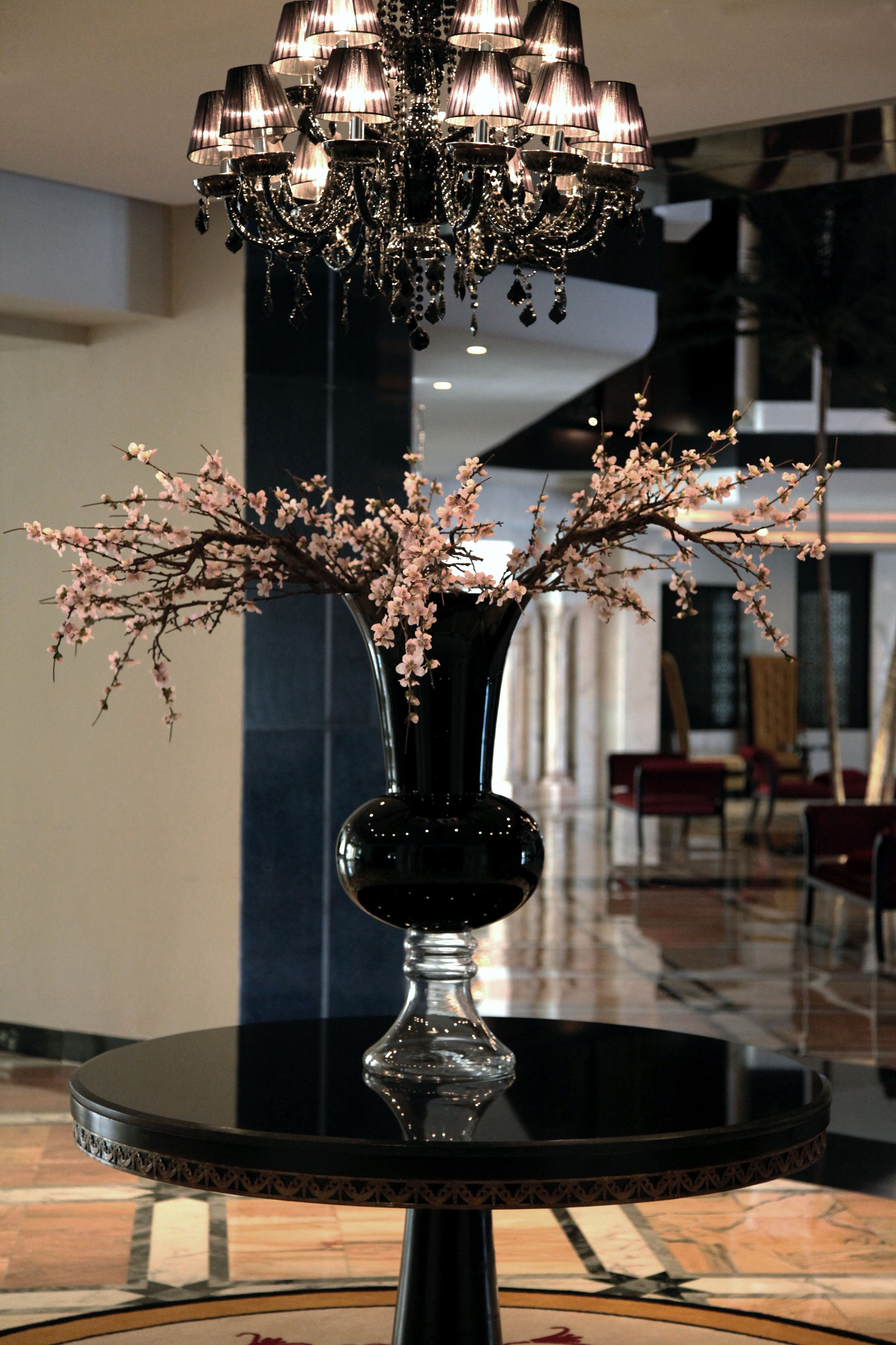 Una mesa negra con un florero de flores rosadas y un candelabro colgante.