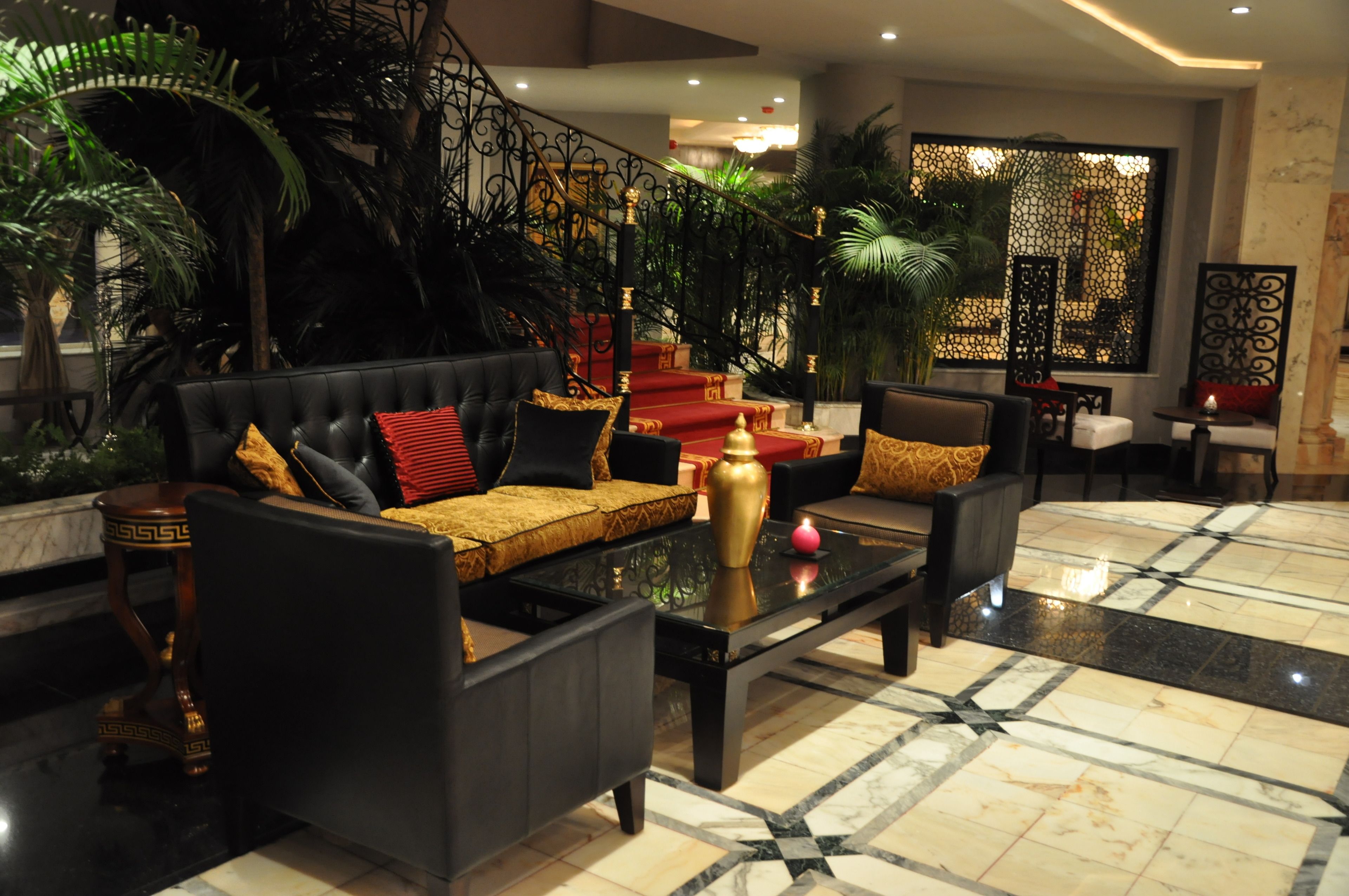 A lobby with a black leather sofa, a glass coffee table, and a red carpeted staircase.