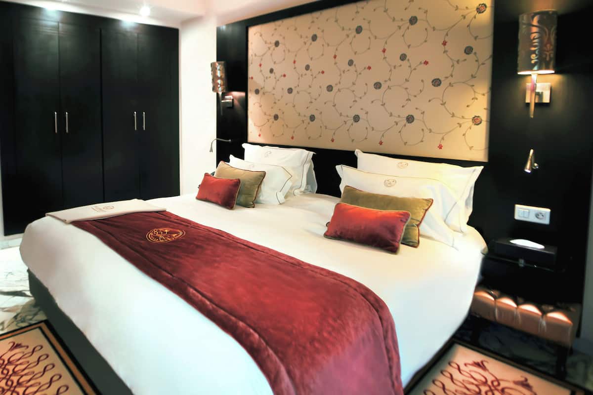 A hotel room with a large bed, dark wooden wardrobe, and a decorative headboard.