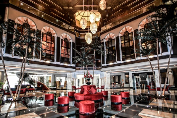 A spacious lobby with a central red seating area, a staircase, and a large chandelier.
