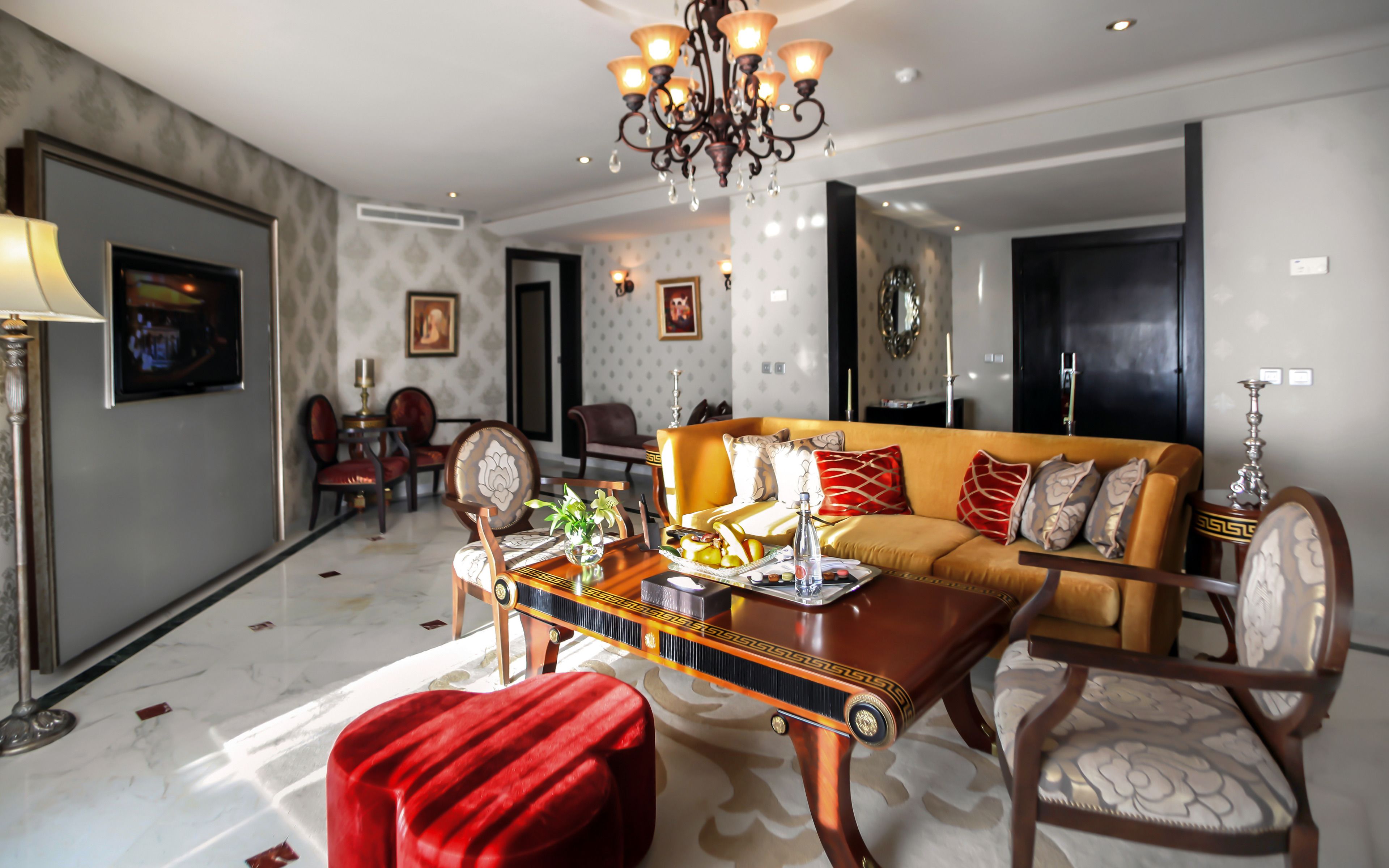 A spacious living room with a modern chandelier, a sofa set, and a dining area with a table set for two.