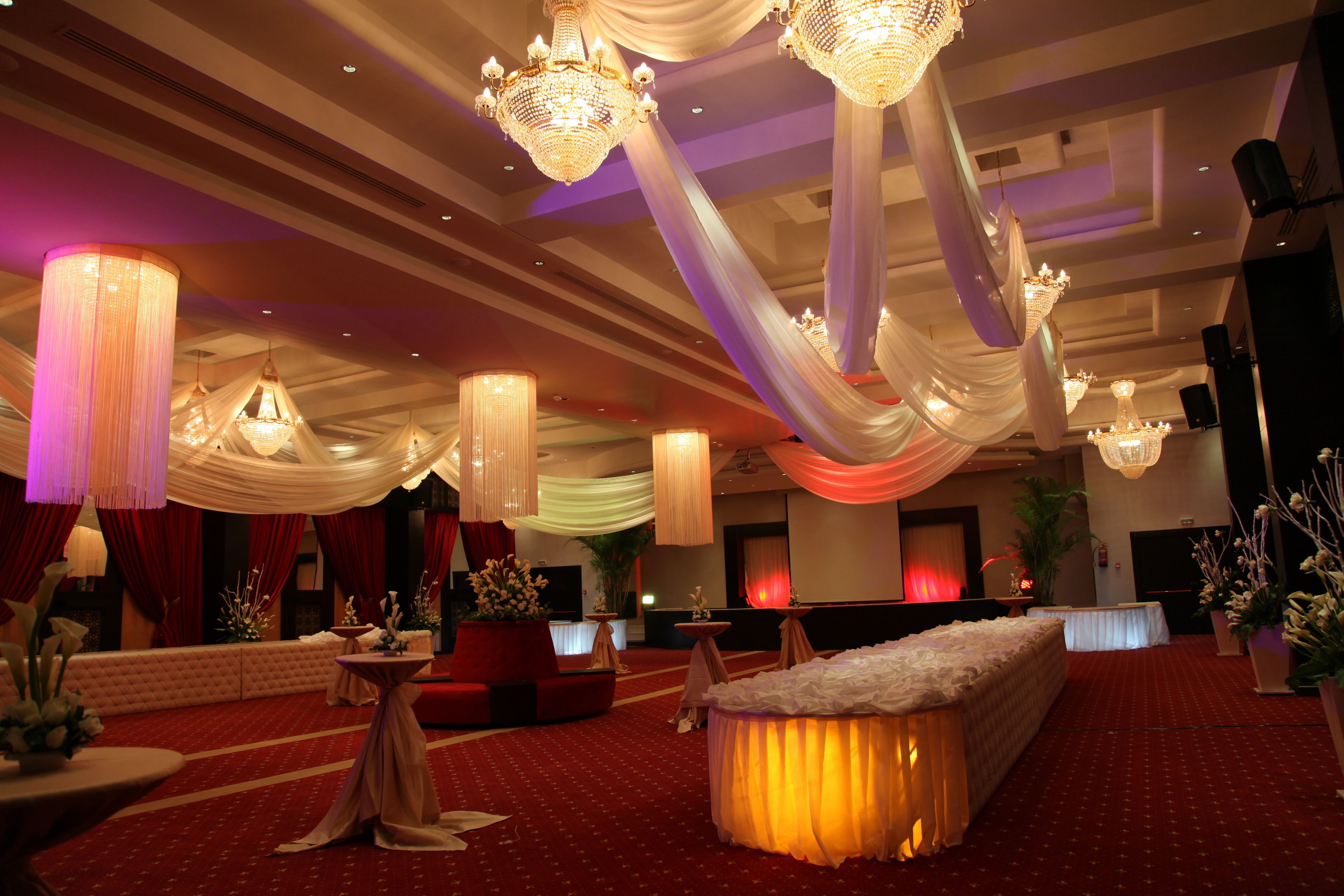 Un salón de banquetes con candelabros, telas decorativas y un escenario.