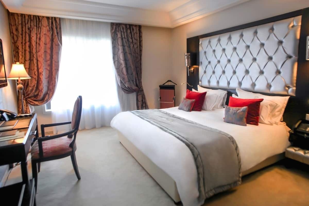 A hotel room with a large bed, a desk, a chair, a wardrobe, and a window with curtains.