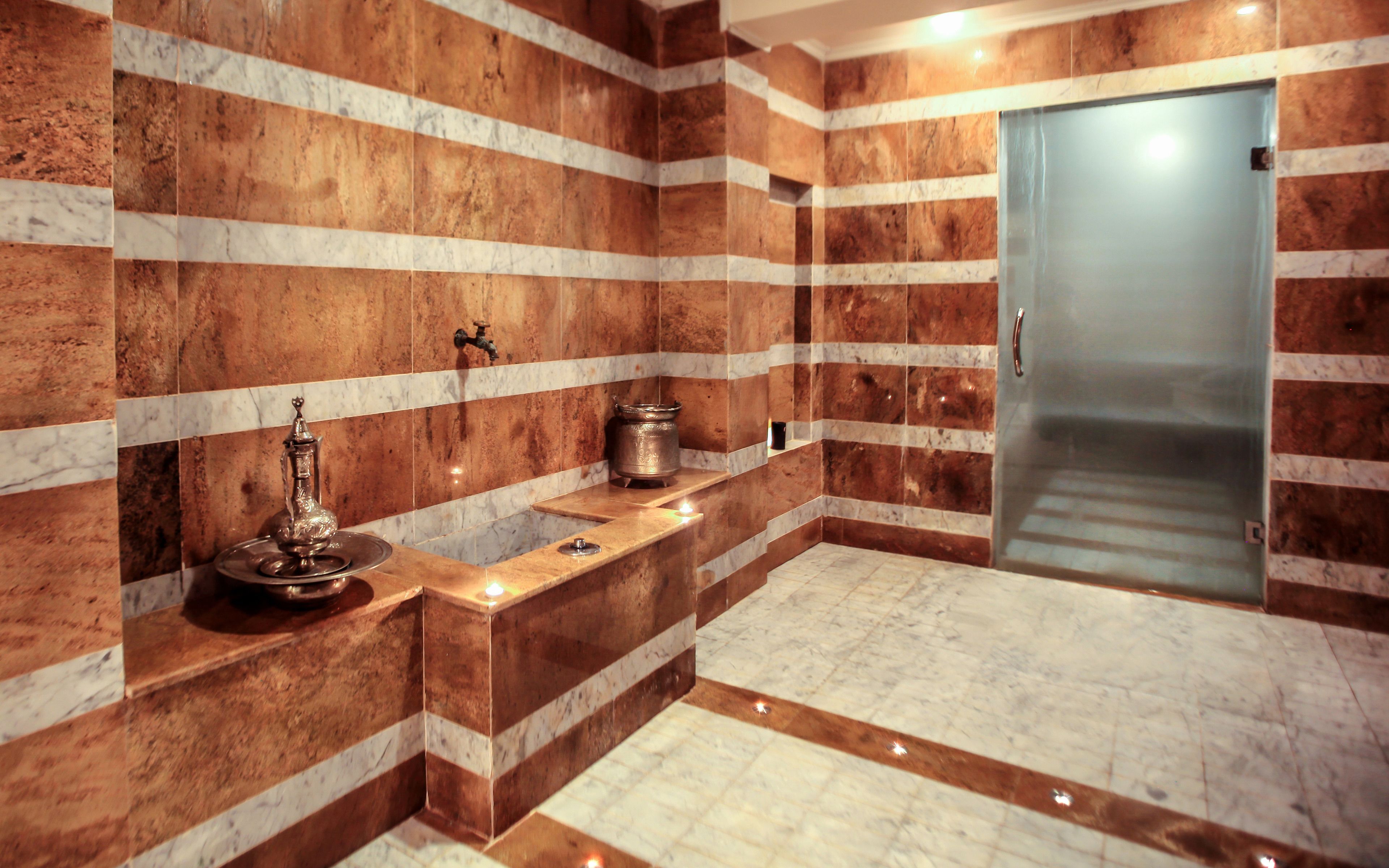 A bathroom with marble walls, a sink, a mirror, and a door.