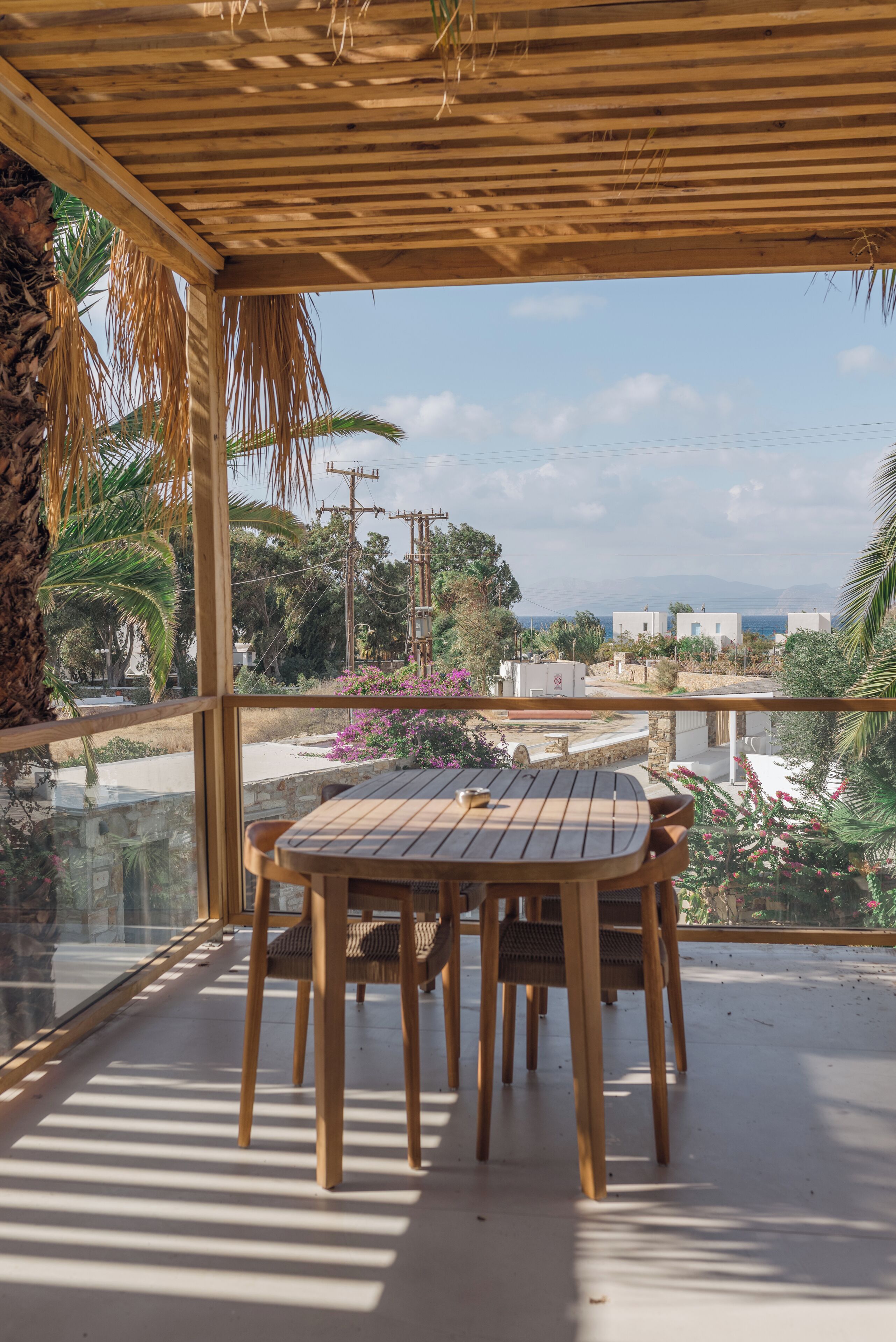A wooden table and chairs on a balcony with a view of buildings and palm trees.