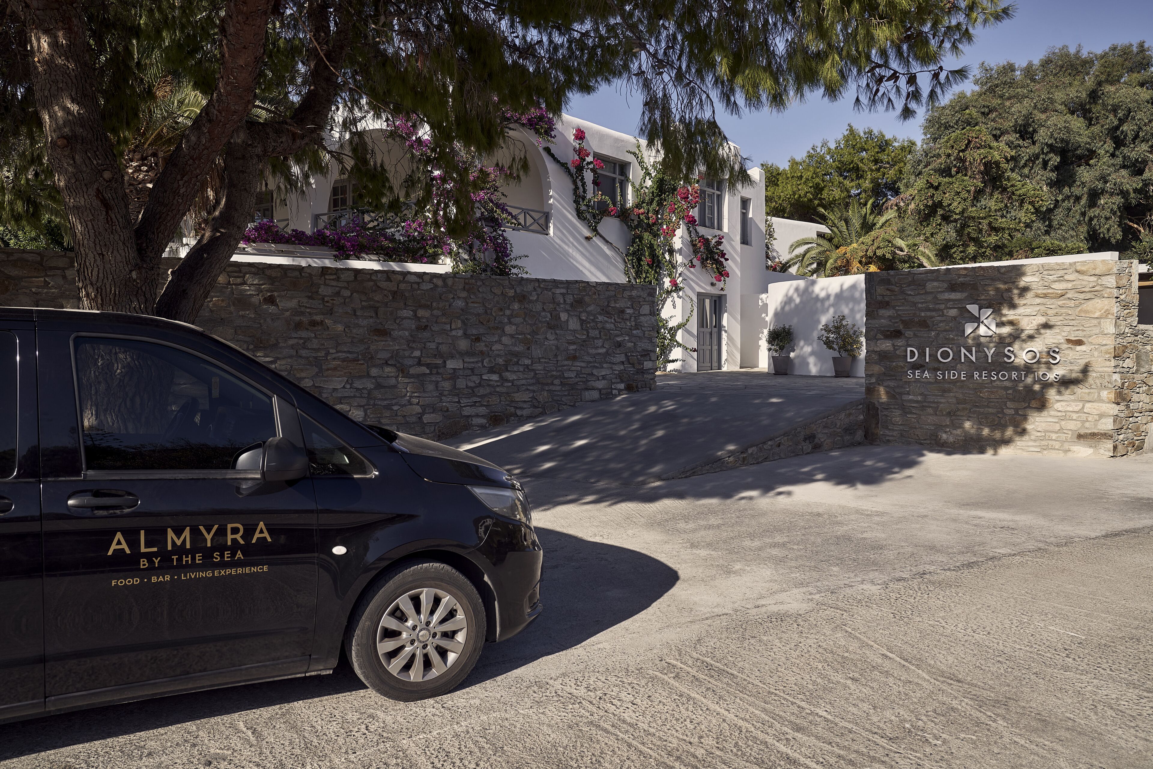 Um carro preto estacionado em frente a uma parede de pedra com uma placa indicando "Dionysos Sea Side Resort 103".