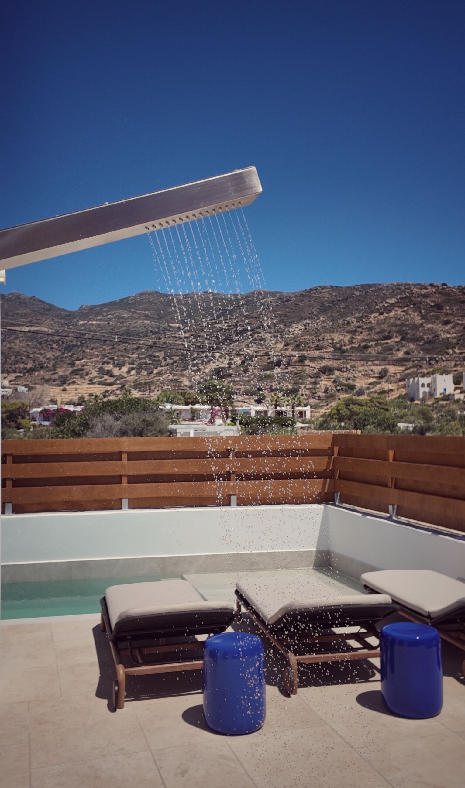 A rooftop pool with a water feature, lounge chairs, and a view of a mountainous landscape.