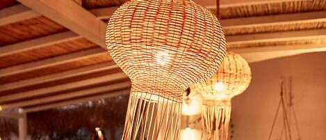 A dining area with a long wooden table set for a meal, hanging woven light fixtures above, and a rustic ceiling.
