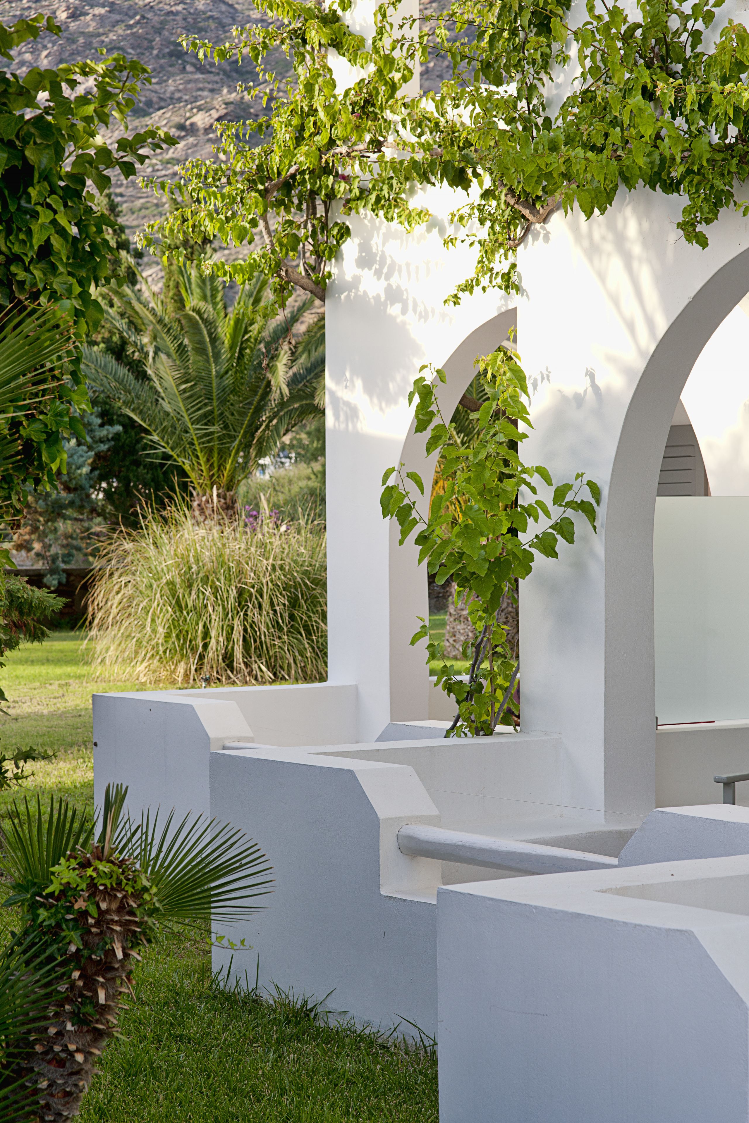 A white building with arched windows and a garden with various plants.