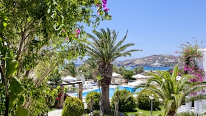 A pool area with palm trees and a view of the sea. - Dionysos Beach Resort & Villas (Ios)